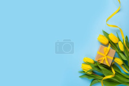 Téléchargez les photos : Yellow tulip flowers and gift box on blue background. Women's day or Mother's day concept. Flat lay, top view - en image libre de droit
