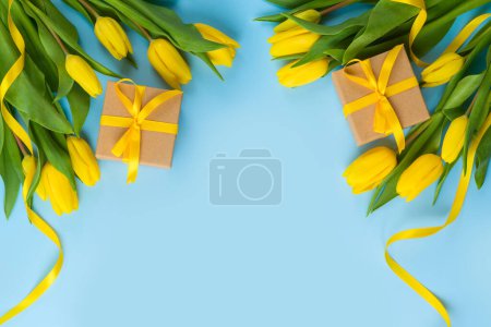 Photo for Yellow tulip flowers and gift box on blue background. Women's day or Mother's day concept. Flat lay, top view - Royalty Free Image