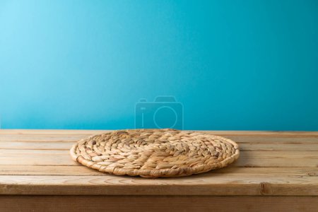 Foto de Mesa de madera vacía con alfombra de mimbre sobre fondo de pared azul. Contador de cocina maqueta para el diseño y la exhibición del producto - Imagen libre de derechos