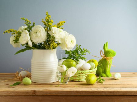 Foto de Bodegón de Pascua con flores blancas ramo y huevos de Pascua decoración en mesa de madera sobre fondo gris - Imagen libre de derechos