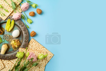 Foto de Fiestas judías Pascua escenario de mesa festiva con matzá, plato de seder y flores de primavera sobre fondo azul. Vista superior, plano - Imagen libre de derechos