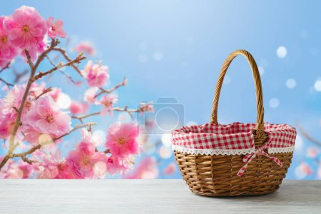 Foto de Cesta de picnic vacía sobre mesa de madera sobre fondo de flores de cerezo. Primavera y Pascua maqueta para el diseño. - Imagen libre de derechos