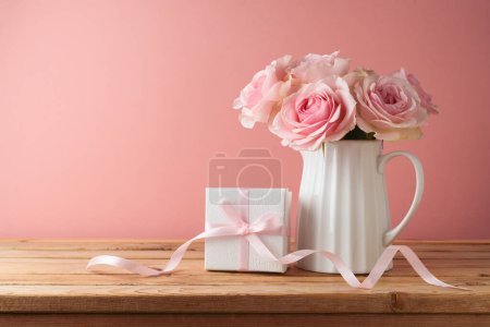 Téléchargez les photos : Joyeux concept de fête des mères avec des fleurs roses et boîte cadeau sur table en bois sur fond rose - en image libre de droit