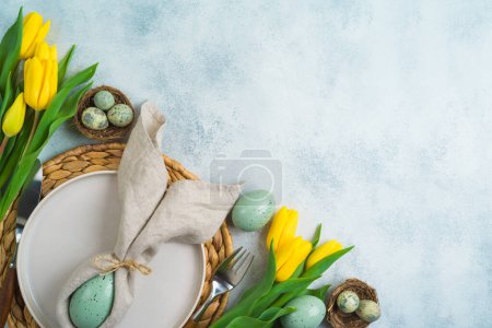Téléchargez les photos : Table de fête de Pâques avec œufs de Pâques, assiette et fleurs de tulipes jaunes sur fond moderne. Vue de dessus, plan plat - en image libre de droit
