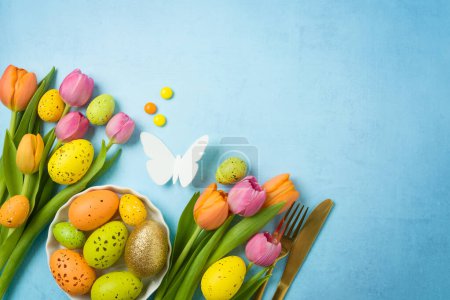Foto de Concepto de celebración de Pascua con huevos de Pascua cubiertos de oro y flores de tulipán sobre fondo azul. Vista superior, plano - Imagen libre de derechos