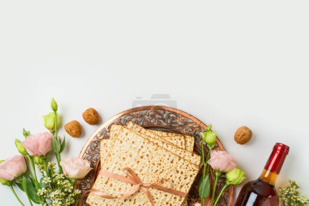Jüdisches Pessach-Konzept mit Matza, Sederteller, Frühlingsblumen und Weinflasche auf weißem Hintergrund. Draufsicht, flache Lage