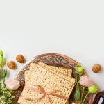 Jewish holiday Passover concept with matzah, seder plate, spring flowers and wine bottle on white  background. Top view, flat lay