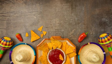 Photo for Mexican party table arrangement with nacho tortilla  chips, maracas and sombrero hat on dark background. Cinco de Mayo holiday celebration. Top view, flat lay - Royalty Free Image