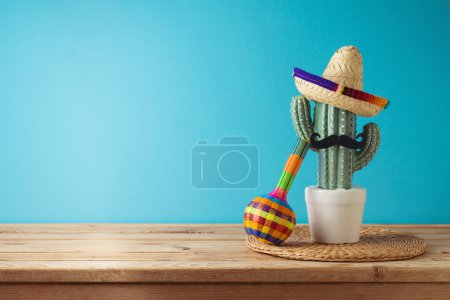Photo for Mexican party concept with cactus, maracas and sombrero hat on wooden table over blue background. Cinco de Mayo holiday celebration - Royalty Free Image