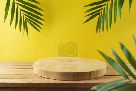 Empty wooden log with palm tree leaves on wooden table over yellow background . Summer mock up for design and product display