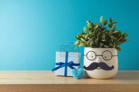 Foto de Concepto del día del padre feliz con linda planta divertida con bigote, gafas y caja de regalo en la mesa de madera sobre fondo azul - Imagen libre de derechos