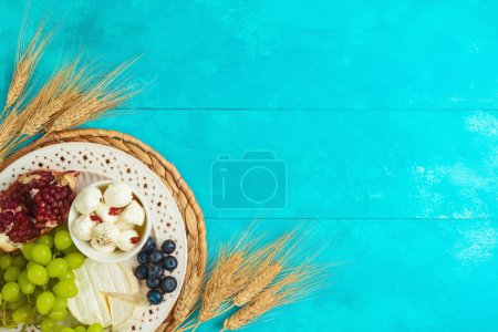 Foto de Fiesta judía Shavuot ajuste de mesa festiva con queso, frutas y espigas de trigo sobre fondo de mesa azul de madera. Vista superior desde arriba - Imagen libre de derechos