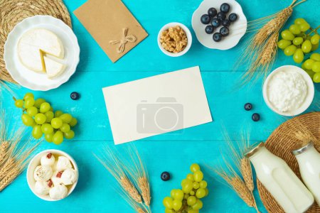 Téléchargez les photos : Carte de vœux Shavuot de vacances juives maquette avec fromage, bouteille de lait et épis de blé sur fond de table bleu en bois. Vue de dessus - en image libre de droit