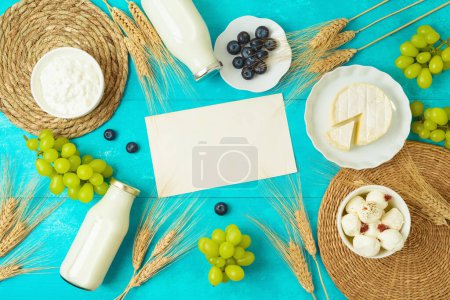 Foto de Fiesta judía Shavuot tarjeta de felicitación maqueta con queso, botella de leche y espigas de trigo sobre fondo de mesa azul de madera. Vista superior desde arriba - Imagen libre de derechos
