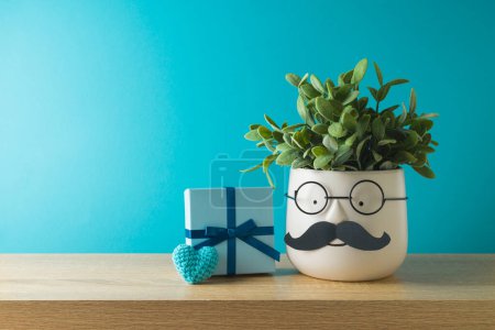 Photo for Happy Father's day concept with cute funny plant,  mustache and gift box on wooden table over blue background - Royalty Free Image