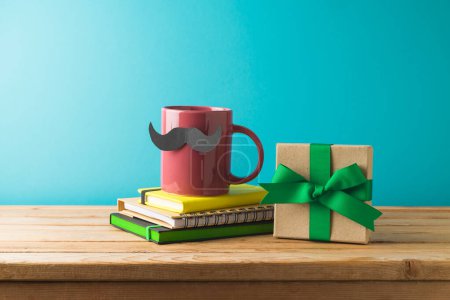 Photo for Happy Father's day concept with colorful coffee cup, mustache, notebook and gift box on wooden table over blue background - Royalty Free Image