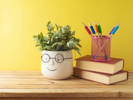 Foto de Volver al concepto de la escuela con lápices de colores, libros y linda planta divertida en la mesa de madera sobre fondo amarillo - Imagen libre de derechos