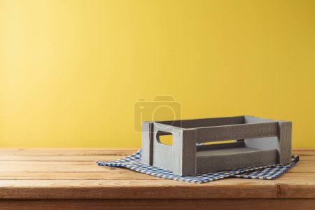 Téléchargez les photos : Boîte en bois vide sur la table avec nappe sur fond mural jaune. Modèle de récolte pour la conception et l'affichage du produit - en image libre de droit