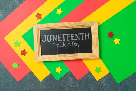 Photo for Juneteenth freedom day concept with colorful paper, blackboard and stars on black background. Top view, flat lay - Royalty Free Image