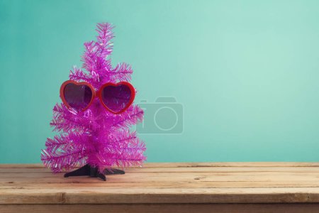 Foto de Concepto de Navidad en julio con divertido árbol de Navidad rosa y gafas de sol en la mesa de madera sobre fondo de menta azul - Imagen libre de derechos