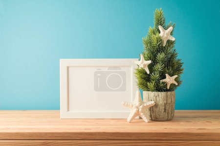 Foto de Concepto de Navidad en julio con árbol de Navidad, marco de la maqueta y estrella de mar en la mesa de madera sobre fondo azul - Imagen libre de derechos