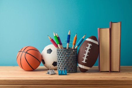 Foto de Concepto de regreso a la escuela con lápices, pelota de baloncesto, pelota de fútbol y libros sobre mesa de madera sobre fondo azul - Imagen libre de derechos