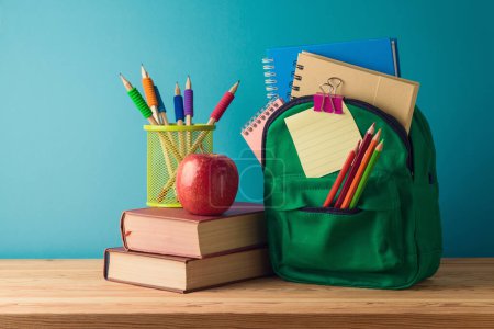 Foto de Concepto de regreso a la escuela con mochila, lápices, libros y manzana sobre mesa de madera sobre fondo azul - Imagen libre de derechos