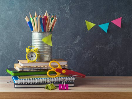 Téléchargez les photos : Retour à l'école avec crayons, cahiers et réveil sur table en bois sur fond de tableau noir - en image libre de droit