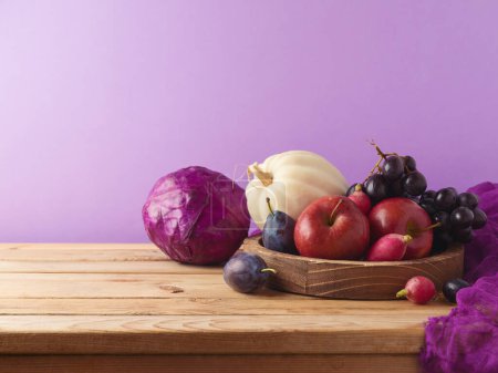 Téléchargez les photos : Concept de récolte d'automne. Citrouille, pomme, raisin et chou rouge sur assiette en bois sur table sur fond violet - en image libre de droit