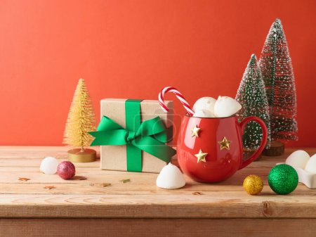 Téléchargez les photos : Tasse de chocolat chaud de Noël avec guimauve, boîte cadeau et décorations sur table en bois sur fond rouge - en image libre de droit