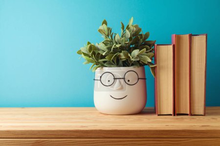 Téléchargez les photos : Concept de retour à l'école avec livres et jolie plante drôle sur table en bois sur fond bleu - en image libre de droit