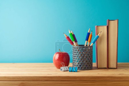 Foto de Volver a la escuela con lápices, libros y manzana sobre una mesa de madera sobre fondo azul - Imagen libre de derechos
