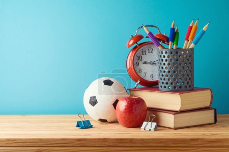 Foto de Volver al fondo de la escuela con lápices, pelota de fútbol, libros, manzana y reloj despertador sobre mesa de madera sobre fondo azul - Imagen libre de derechos