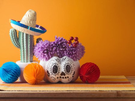Photo for Day of the dead holiday concept. Sugar skull Halloween pumpkin and Mexican party decorations on wooden table over orange background - Royalty Free Image