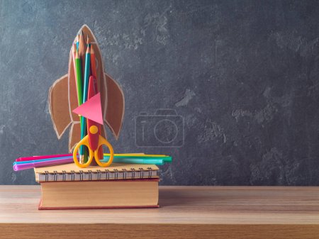 Foto de Concepto de regreso a la escuela con cohete, lápices, cuaderno y libro sobre mesa de madera sobre fondo de pizarra - Imagen libre de derechos