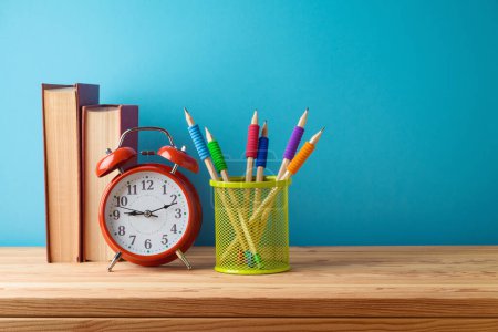 Téléchargez les photos : Bureau à domicile fond avec crayons, livres et réveil sur table en bois sur fond bleu - en image libre de droit