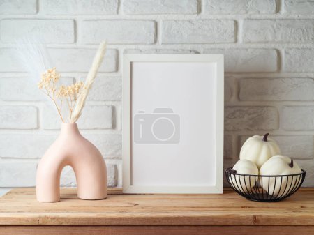 Photo for Poster frame mock up for Autumn season.Modern vase and pumpkin decoration on wooden table over brick wall background - Royalty Free Image