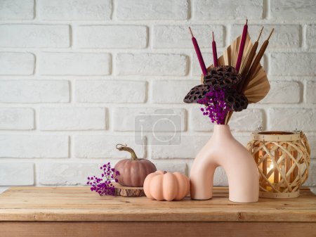 Photo for Autumn season concept with dried bouquet in modern vase and pumpkin decoration on wooden table over brick wall background - Royalty Free Image