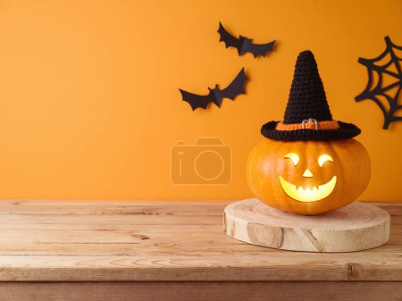 Téléchargez les photos : Halloween Jack o lanterne citrouille décoration sur table en bois sur fond mural orange. Modèle de vacances pour le design et l'affichage des produits - en image libre de droit