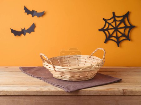 Photo for Empty basket with tablecloth on wooden table over orange wall and paper decorations background. Halloween mock up for design and product display. - Royalty Free Image