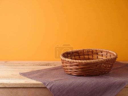 Foto de Cesta vacía con mantel sobre mesa de madera sobre fondo de pared naranja. Burla de Halloween o Acción de Gracias para el diseño y la exhibición del producto. - Imagen libre de derechos