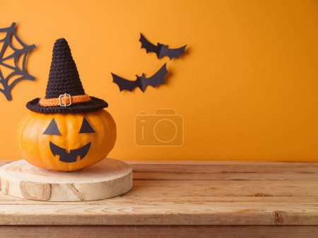 Téléchargez les photos : Halloween Jack o lanterne citrouille décoration sur table en bois sur fond mural orange. Modèle de vacances pour le design et l'affichage des produits - en image libre de droit