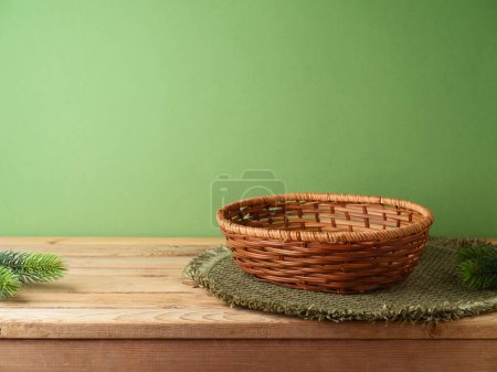 Foto de Cesta vacía con alfombra de lugar en la mesa de madera sobre la pared verde y fondo de decoración de pinos. Maqueta de Navidad para el diseño y la exhibición del producto. - Imagen libre de derechos