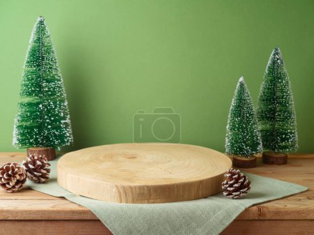 Foto de Podio de tronco vacío con mantel sobre mesa de madera sobre pared verde y fondo de decoración de pino. Maqueta de Navidad para el diseño y la exhibición del producto. - Imagen libre de derechos