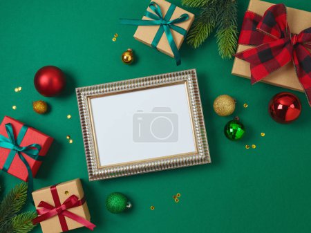 Photo for Christmas and New Year picture frame mock up with gift box and decorations on green background. Top view, flat lay - Royalty Free Image
