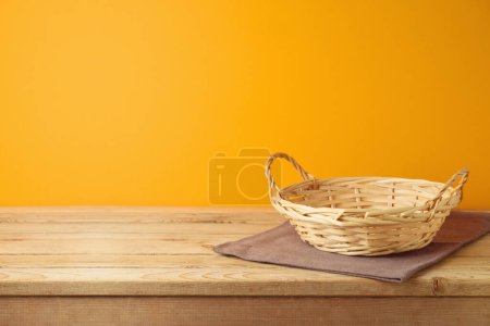 Foto de Cesta vacía con mantel sobre mesa de madera sobre fondo de pared naranja. Simulación de acción de gracias para el diseño y la exhibición del producto - Imagen libre de derechos
