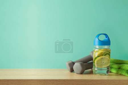 Photo for Fitness background with infused water bottle, towel and dumbbells on wooden table over blue background - Royalty Free Image