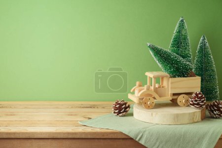 Foto de Mesa de madera con decoración de pino y camión de juguete sobre fondo verde. Navidad e invierno se burlan de las vacaciones para el diseño y la exhibición del producto - Imagen libre de derechos