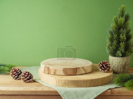 Foto de Podio de tronco vacío con mantel sobre mesa de madera sobre pared verde y fondo de decoración de pino. Maqueta de Navidad para el diseño y la exhibición del producto. - Imagen libre de derechos