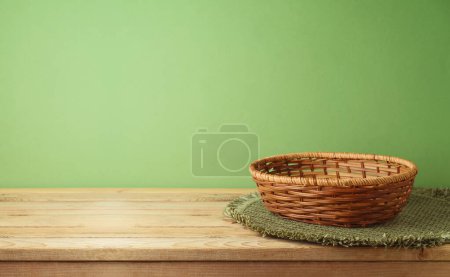 Téléchargez les photos : Panier vide avec tapis de place sur table en bois sur fond mural vert. Modèle de cuisine pour la conception et l'affichage du produit. - en image libre de droit